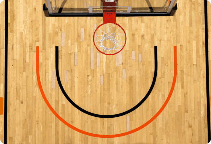 Overhead view of a basketball hoop and court, showing the free-throw line and key area with red and black markings on a wooden floor.